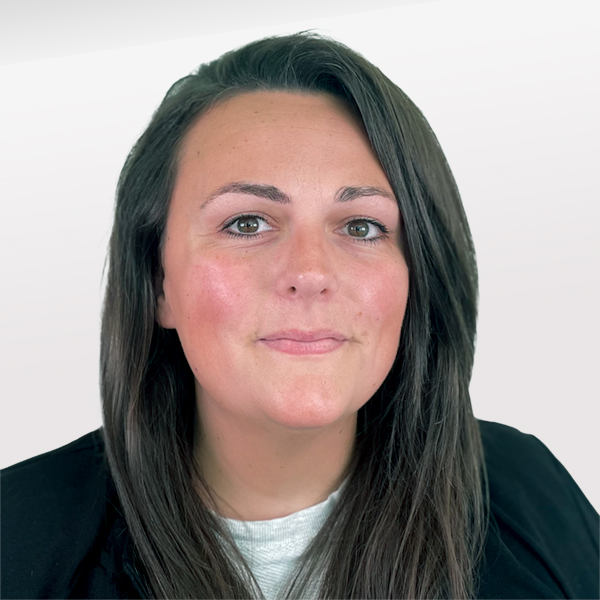 Photo en noir et blanc d'une femme aux longs cheveux ondulés et portant des lunettes, souriant doucement devant un fond blanc texturé.