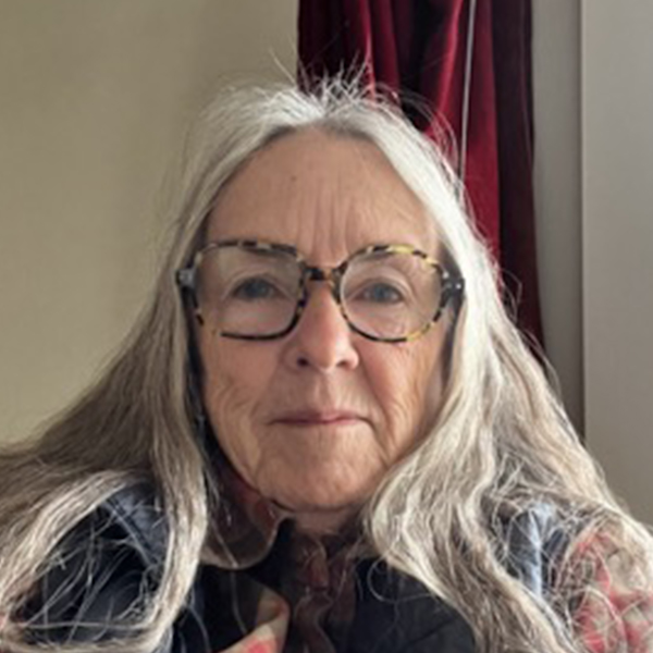 Professional headshot of a smiling man with short hair, glasses, and a checkered suit jacket over a white shirt and dark tie, in front of a grey background.
