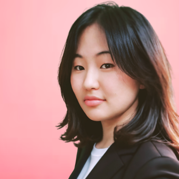 Professional headshot of a smiling man with short hair, glasses, and a checkered suit jacket over a white shirt and dark tie, in front of a grey background.